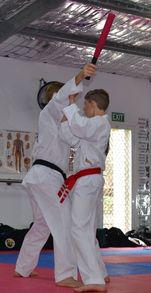 A Man in a White Karate Uniform is Holding a Red Bat — Him-Do Tae Kwon Do Academy In Salamander Bay, NSW