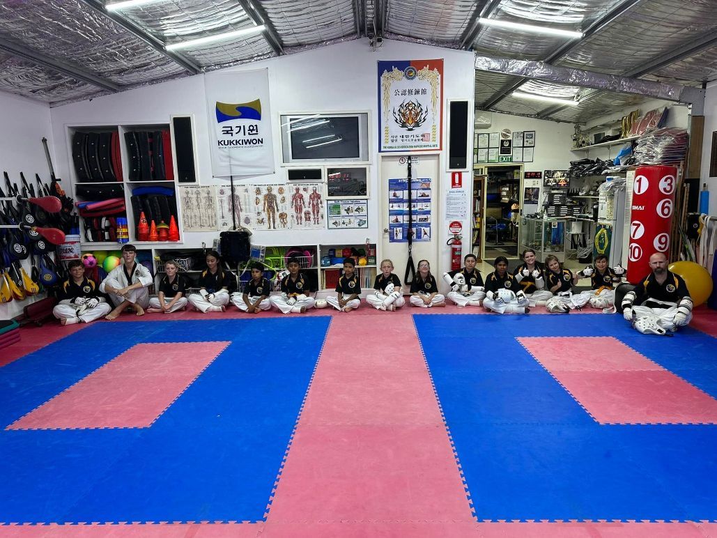 A Group of Children Are Sitting on a Karate Mat in a Gym — Him-Do Tae Kwon Do Academy In Salamander Bay, NSW