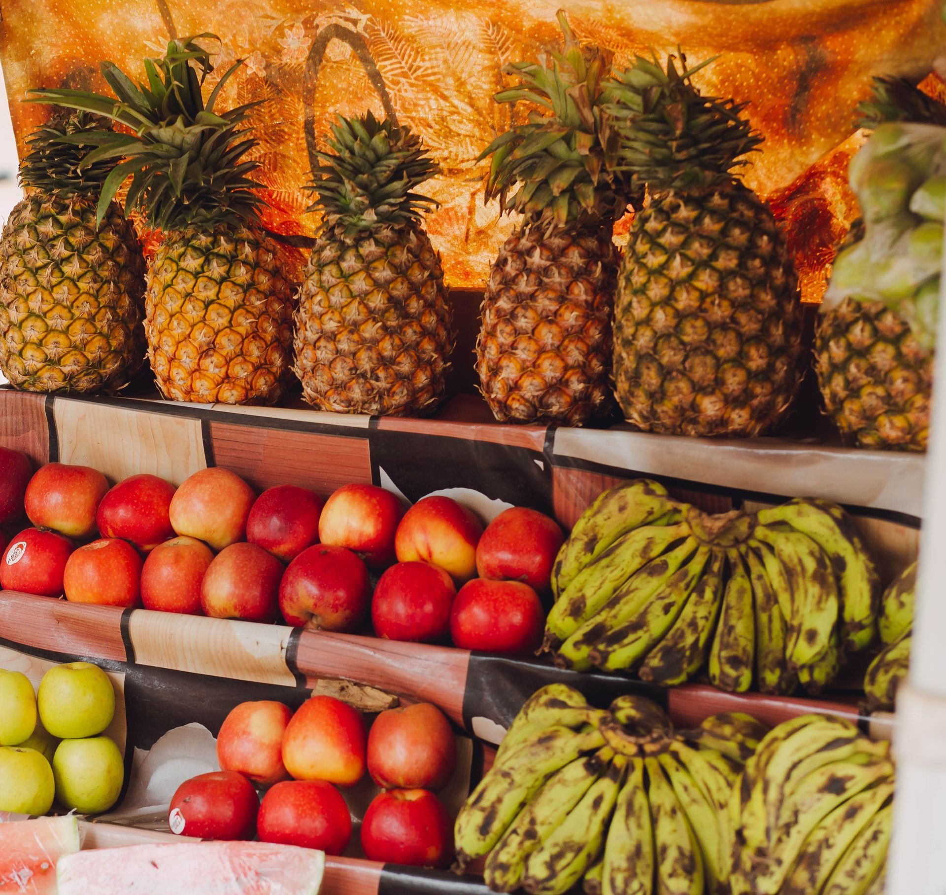 Market display of pineapples, bananas, apples, and pears on stacked shelves