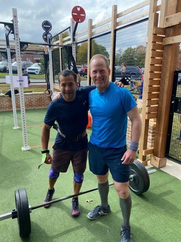 Two men are posing for a picture in a gym with a barbell.