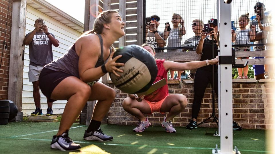 A woman is squatting down while holding a medicine ball.