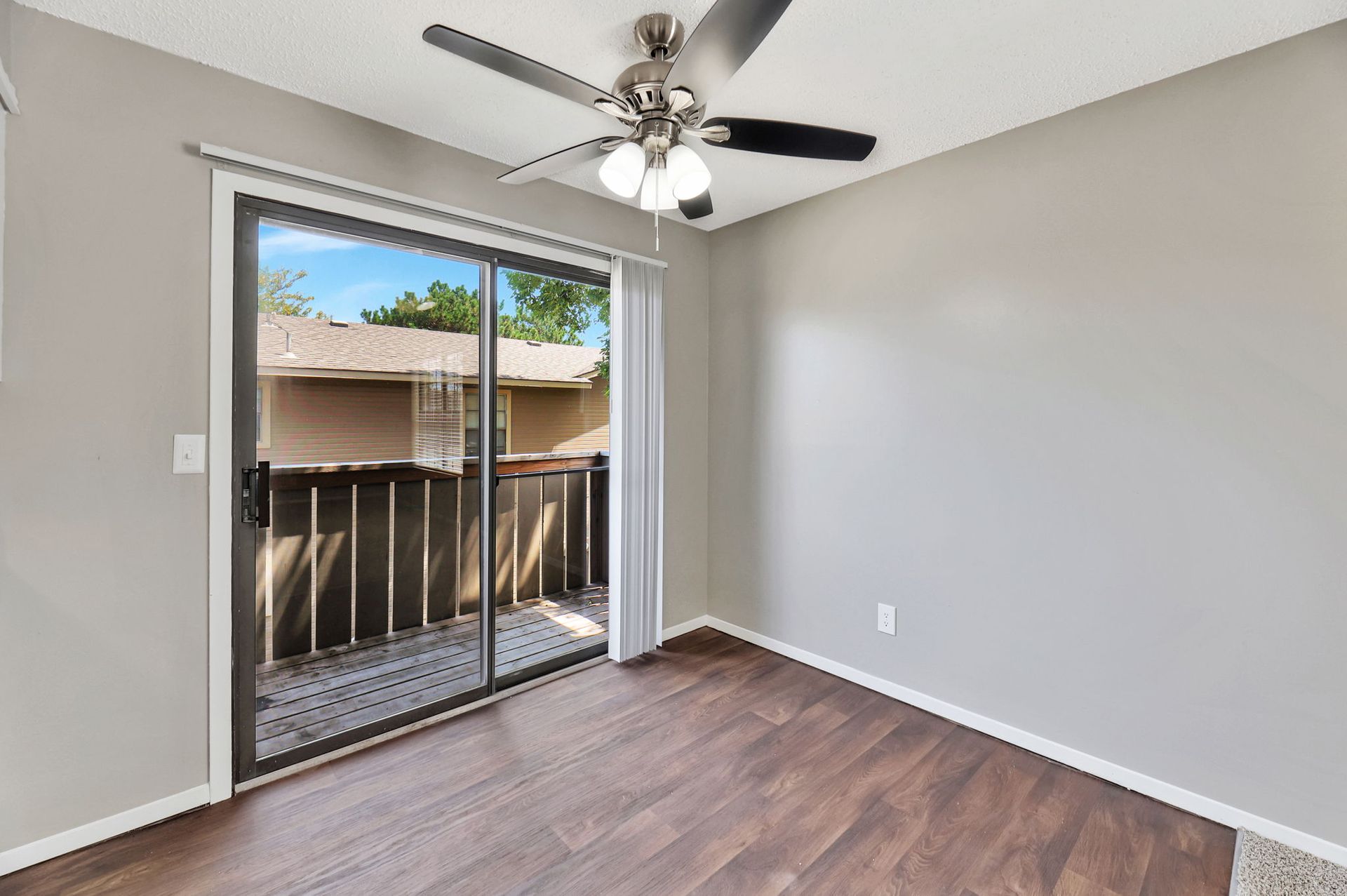 An empty living room with a ceiling fan and sliding glass doors leading to a balcony.