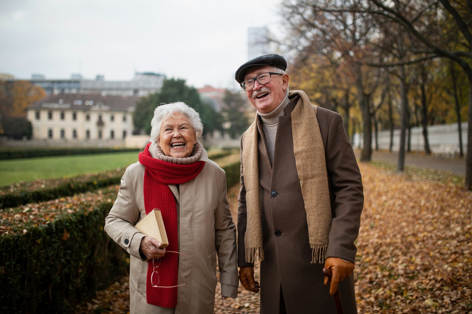 An elderly couple is sitting on a couch laughing and drinking coffee.