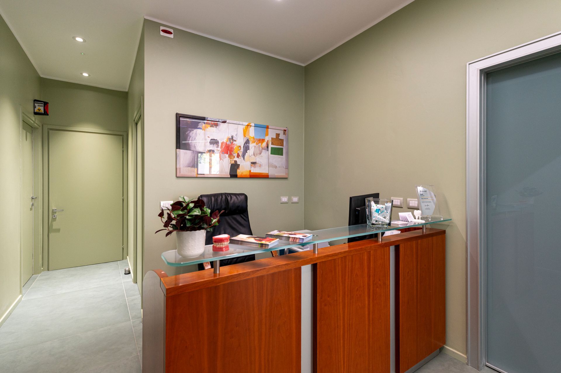 Banco della reception in uno studio medico; mobili in legno, piano in vetro, opere d'arte astratte alle pareti, pareti verdi.