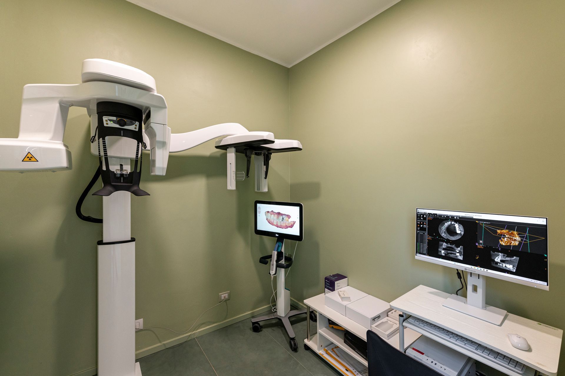 Studio dentistico con apparecchio per radiografie panoramiche e monitor che visualizzano le scansioni.