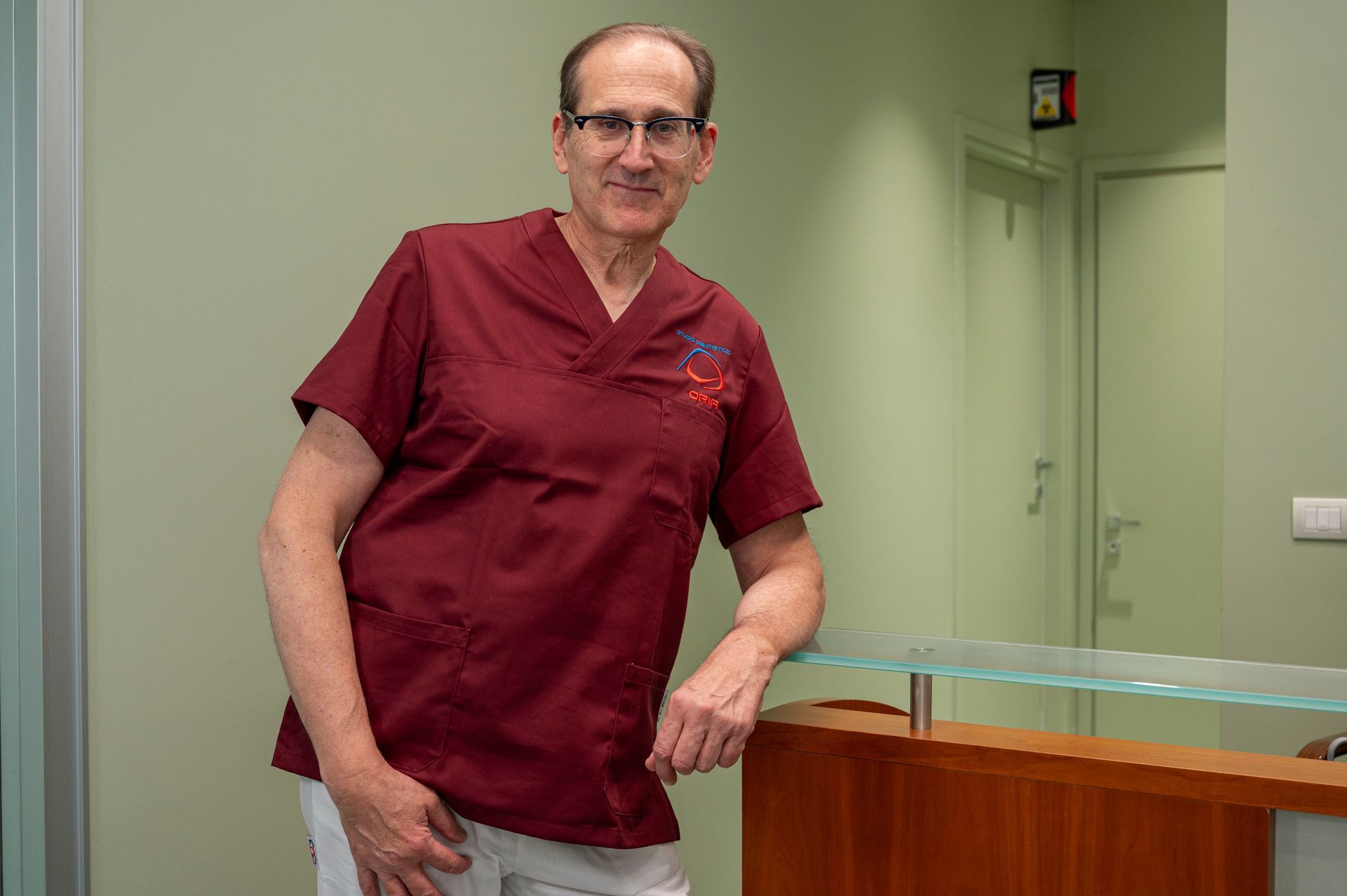 Un uomo in camice color marrone si appoggia alla reception di una clinica.