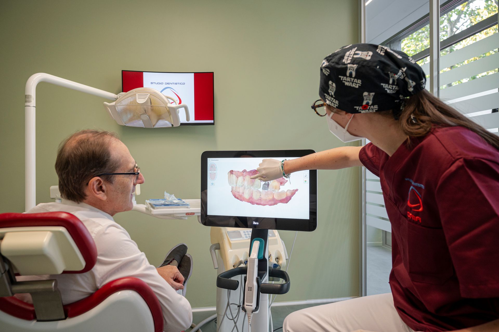 Un dentista indica un modello dentale digitale sullo schermo mentre spiega a un paziente seduto sulla poltrona del dentista.