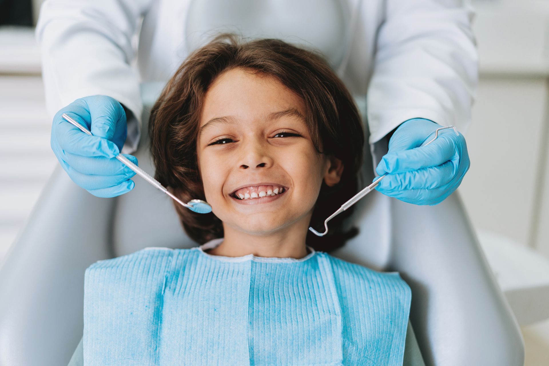 Bambino sorridente sulla poltrona del dentista; il dentista con guanti e strumenti controlla i denti.