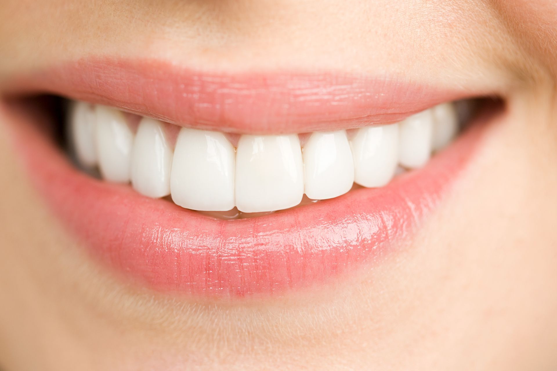 Primo piano del sorriso di una persona, che mostra denti bianchi e dritti e labbra rosa.