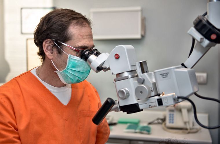 Un medico in camice arancione e mascherina osserva attraverso un microscopio in uno studio medico.