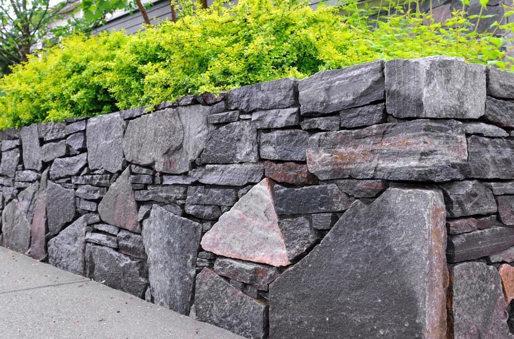 A Stone Wall is Surrounded by Trees and Bushes on a Sidewalk — Gears Excavation In Cedar Pocket, QLD