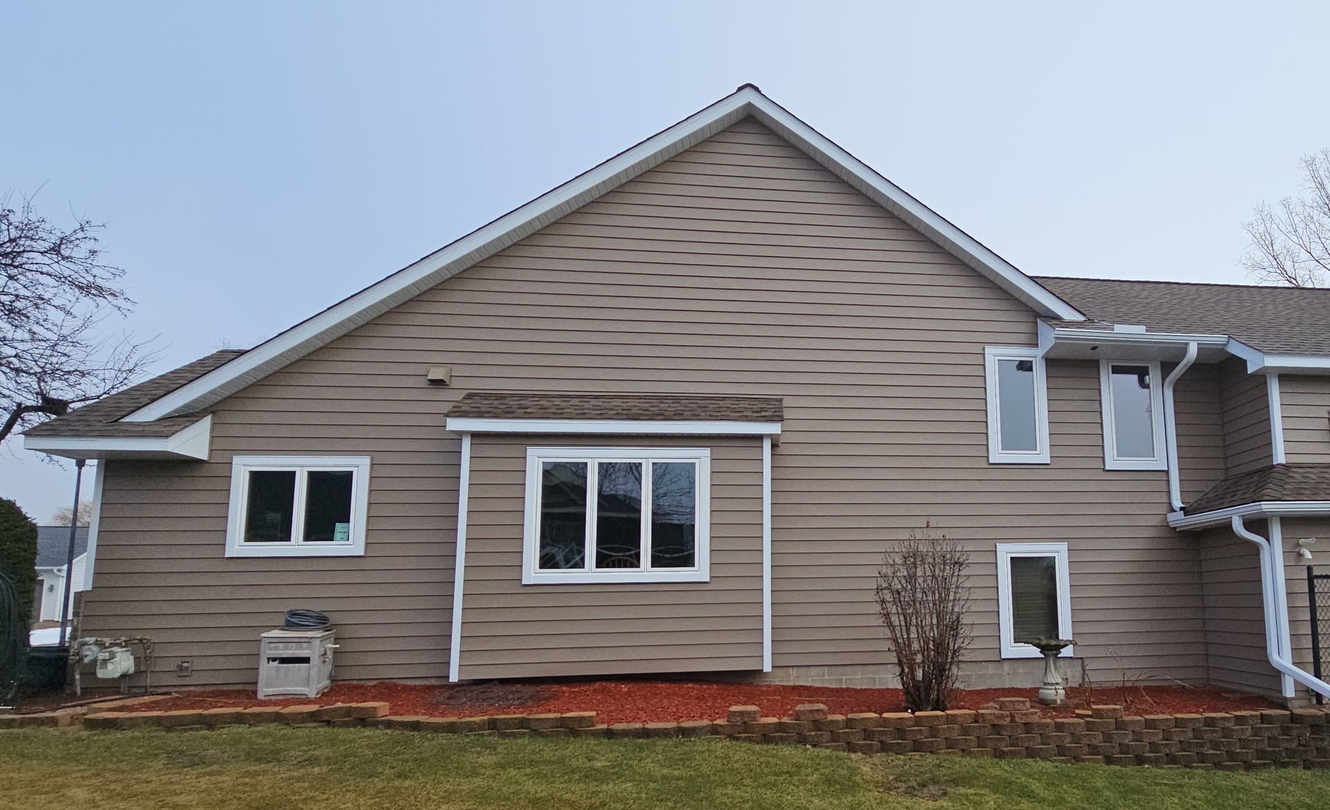 Beige suburban house exterior with white trim and multiple windows on an overcast day