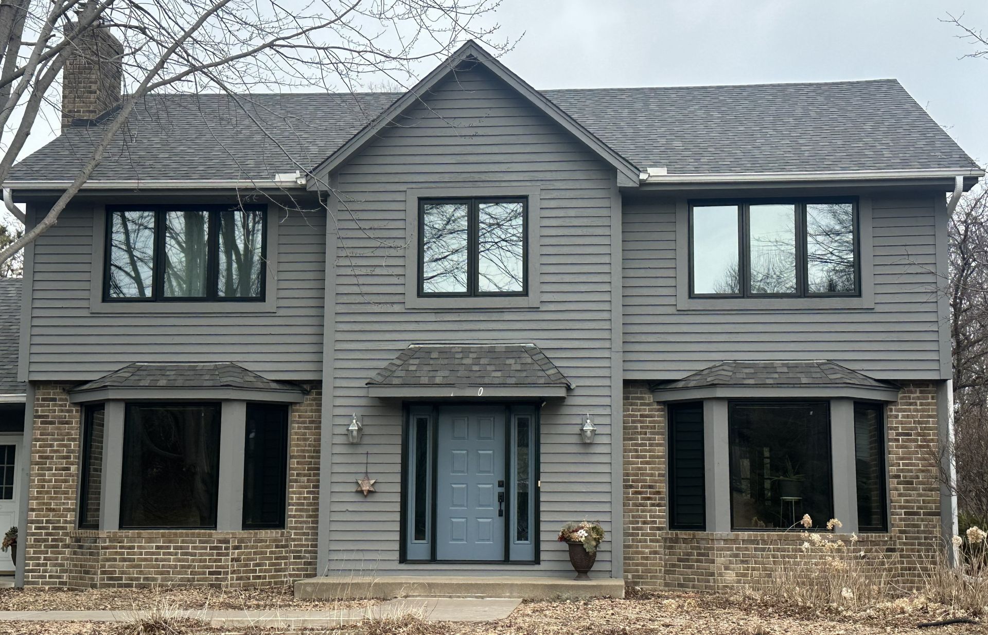 Two-story gray house with stone accents, a double front door, and large windows in a winter setting