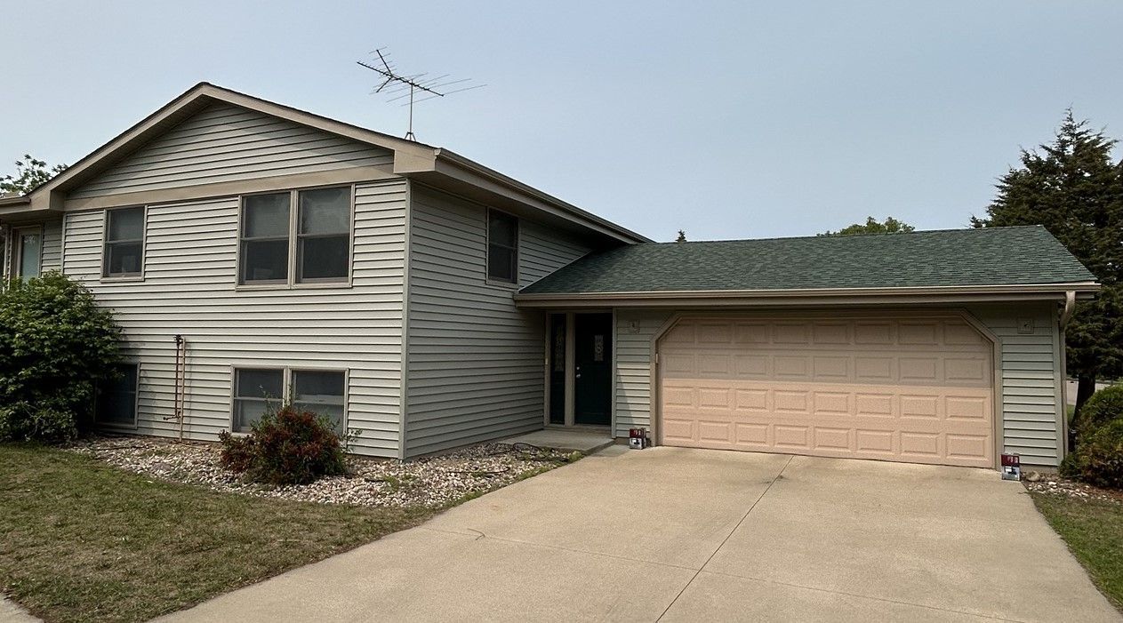 Suburban two-story house with beige siding, attached garage, and a concrete driveway under a cloudy sky
