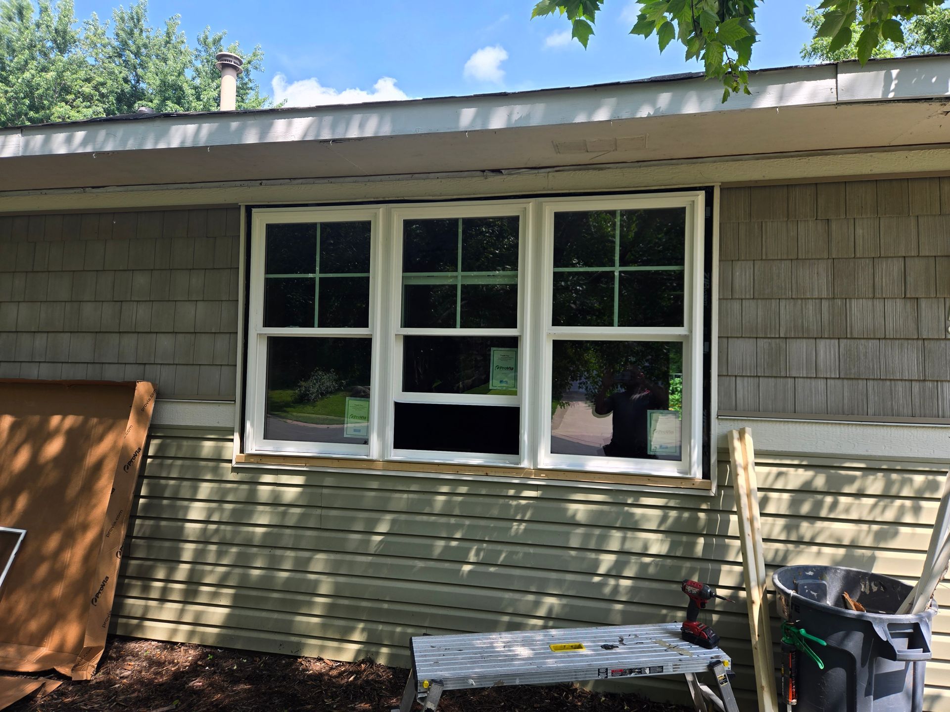 House exterior with three windows, gray siding, and a cluttered yard with tools and boards.