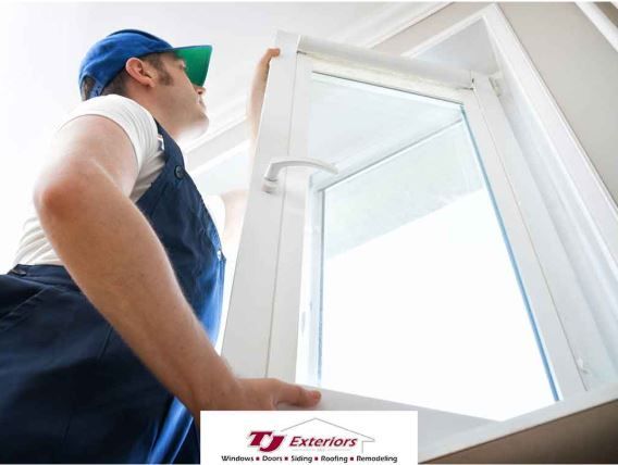 Man in overalls installing a white window, looking upwards.