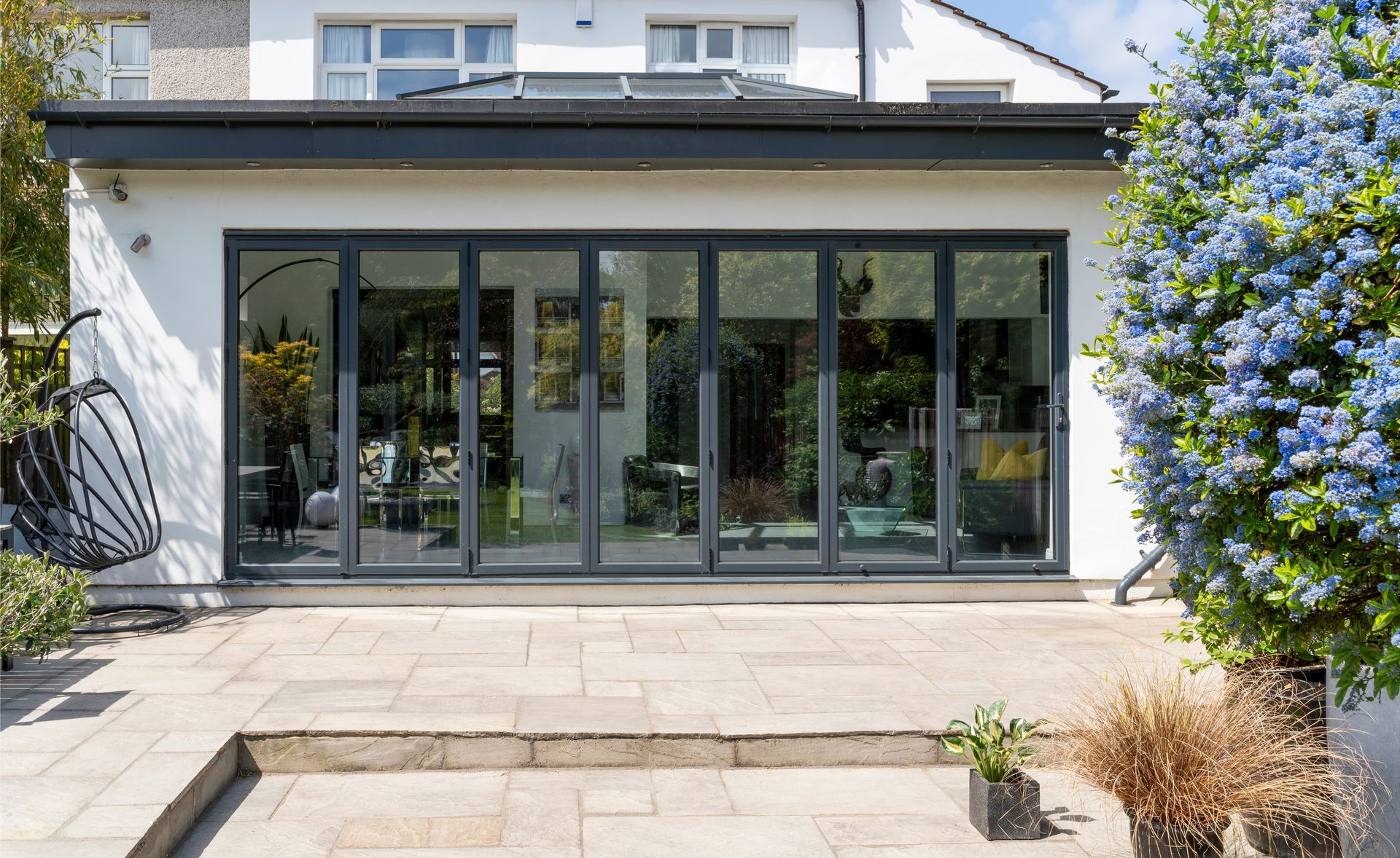 Modern home extension with glass folding doors opening onto a paved patio. Modern home extension with glass folding doors opening onto a paved patio.
