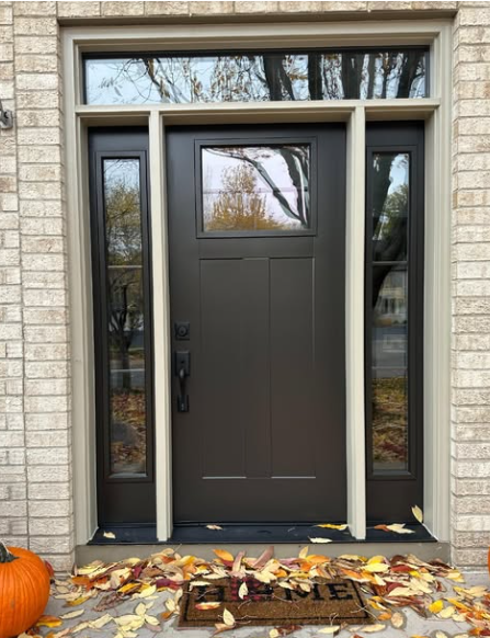 Brown front door with sidelights, autumn leaves, and a pumpkin.