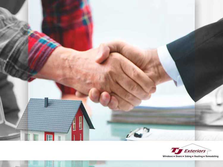 Two people shaking hands over a miniature house, possibly a construction deal.