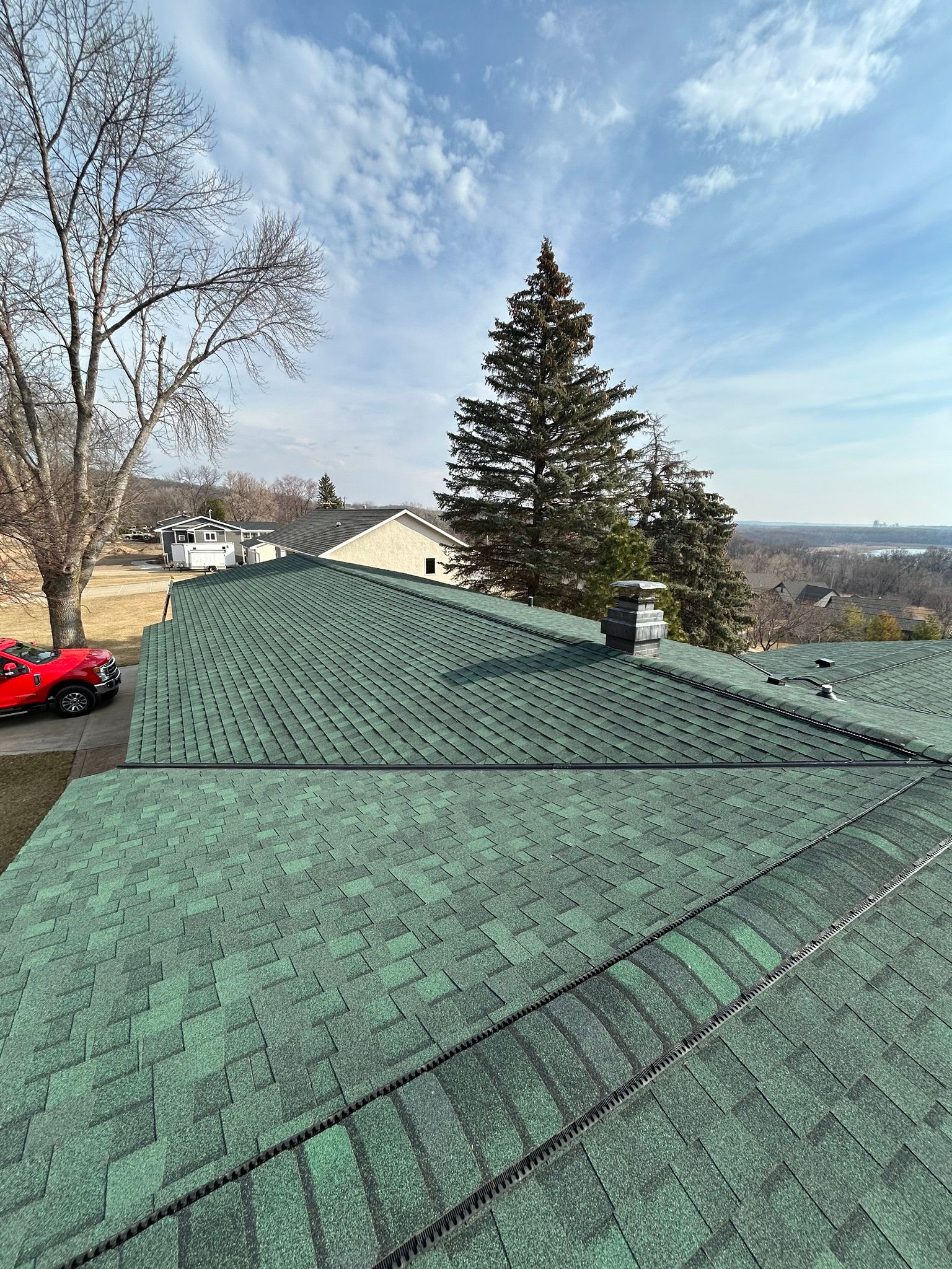 Green shingled roof overlooking trees, houses, and a distant valley on a clear day