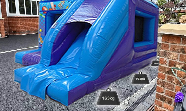 red and blue Bouncy castle on hard standing with sandbags and strapped to a car.