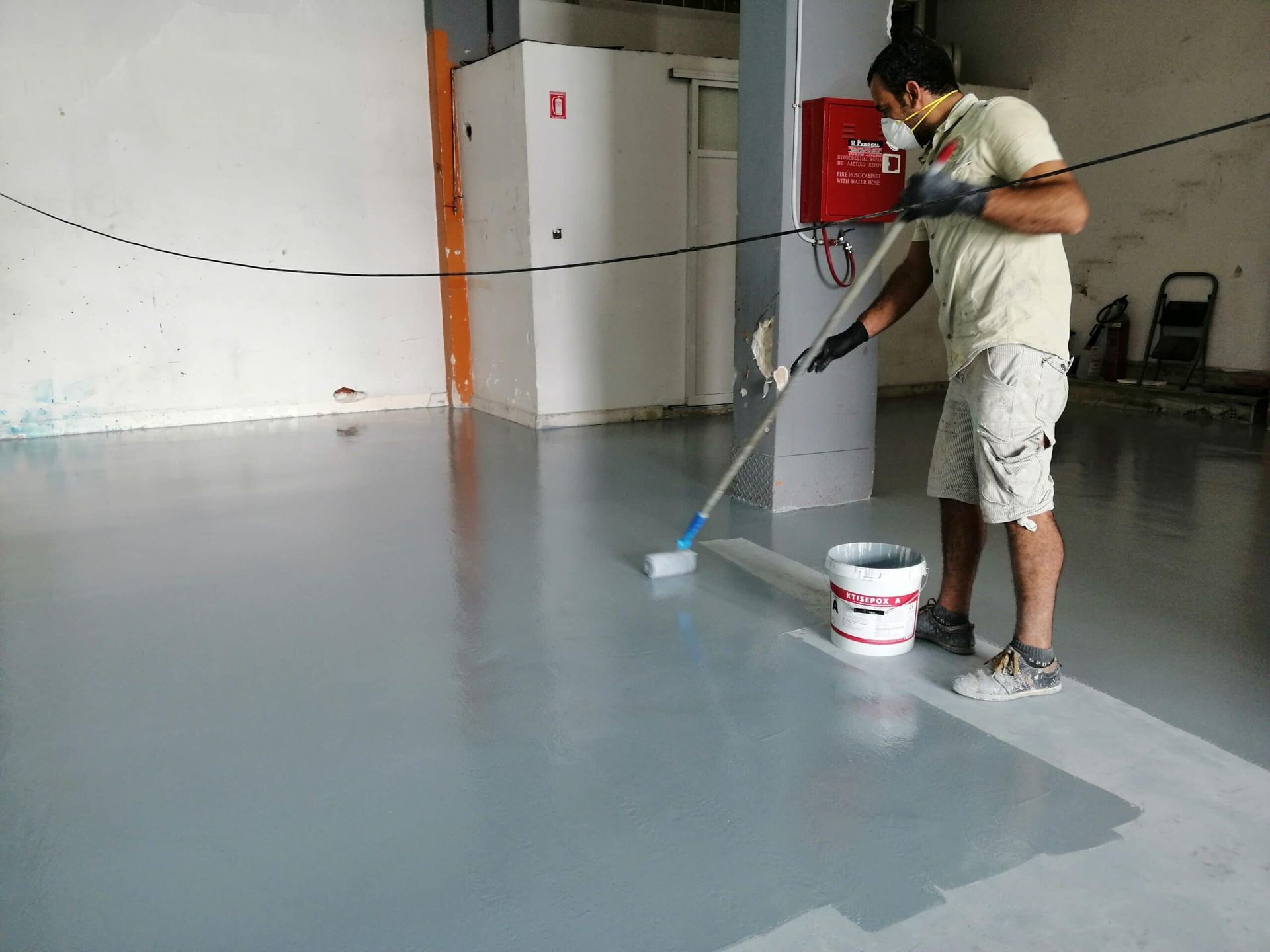 A man is painting a floor with a roller.