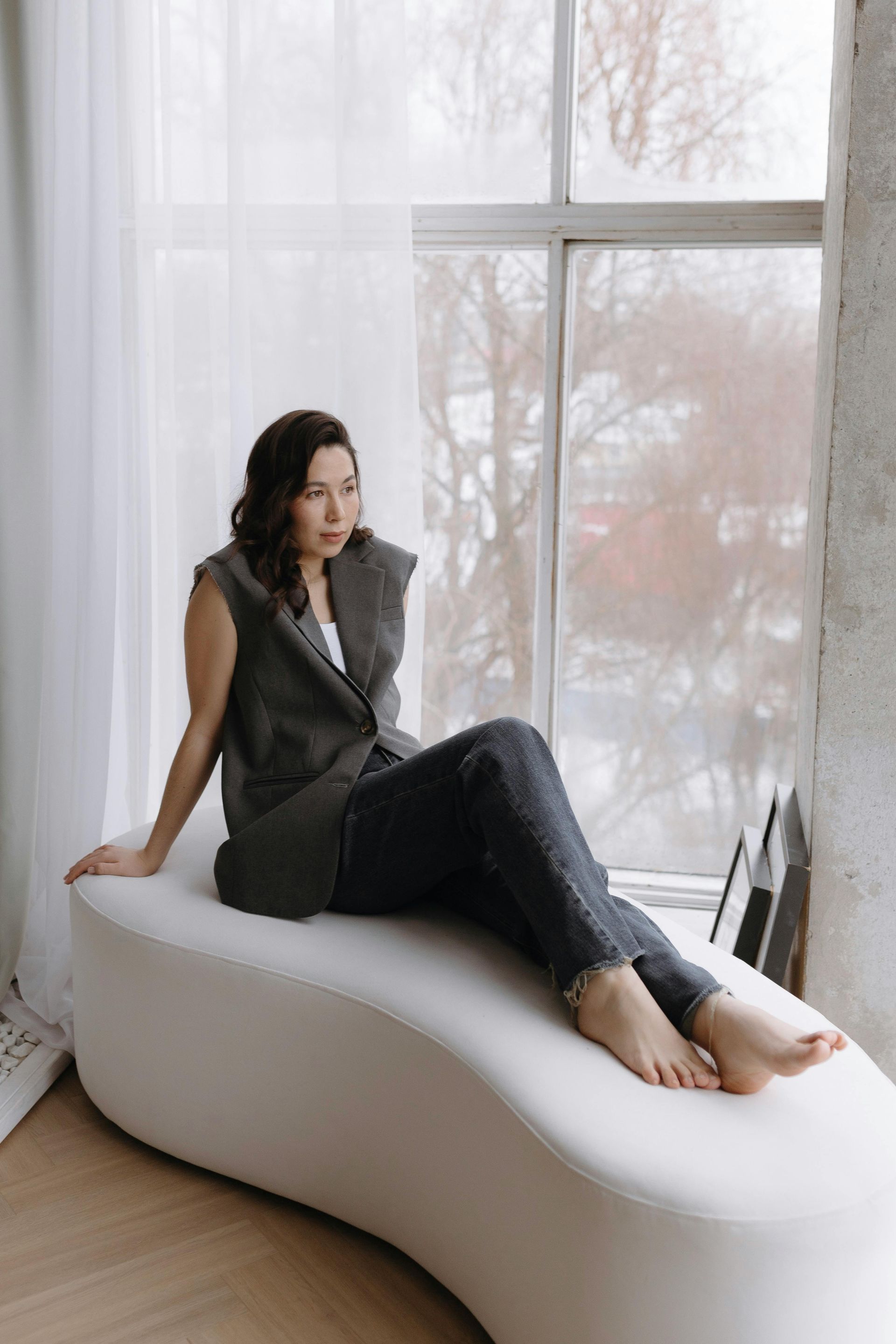 A woman is sitting on a white bench in front of a window.