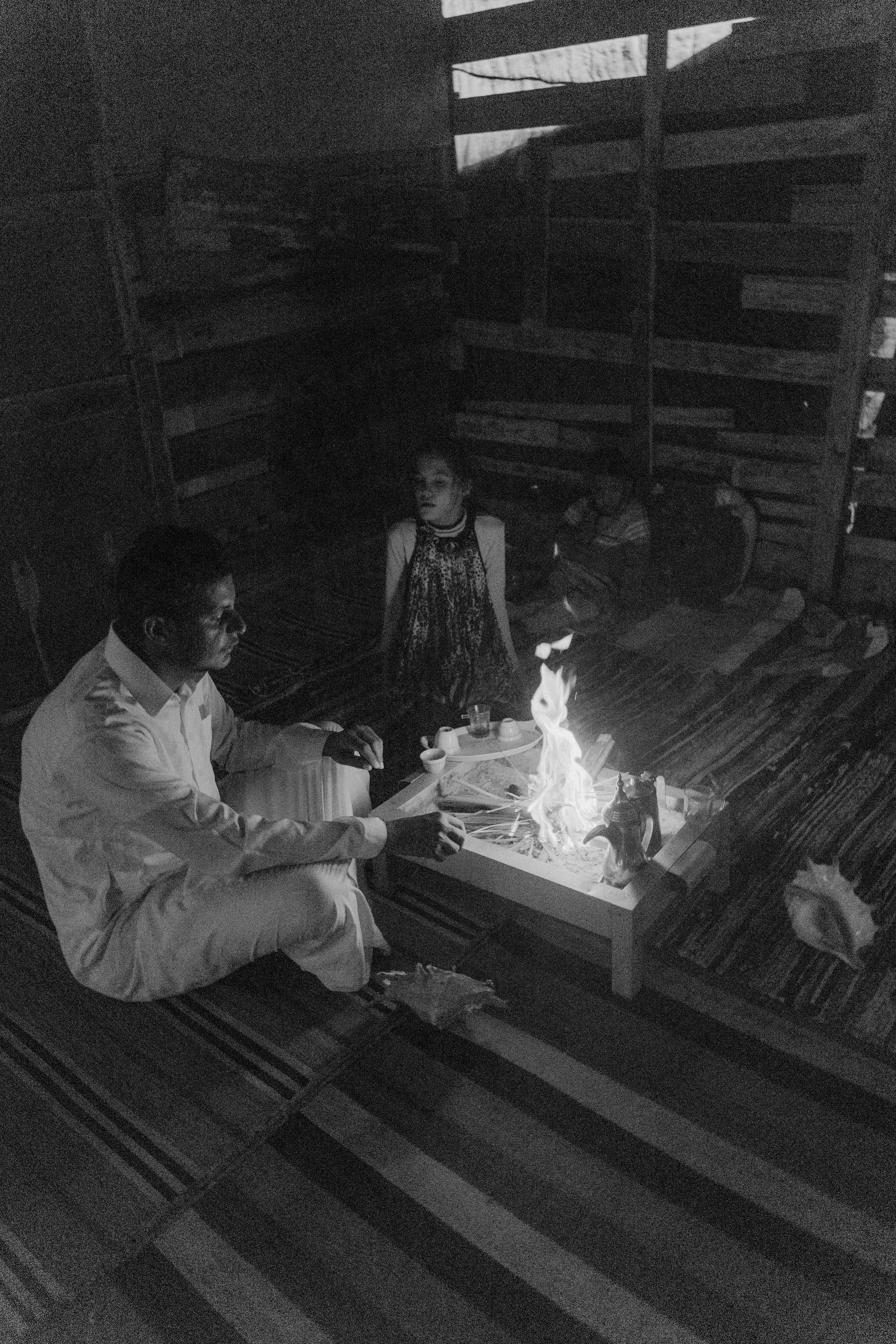 A man and a woman are sitting around a fire in a black and white photo.