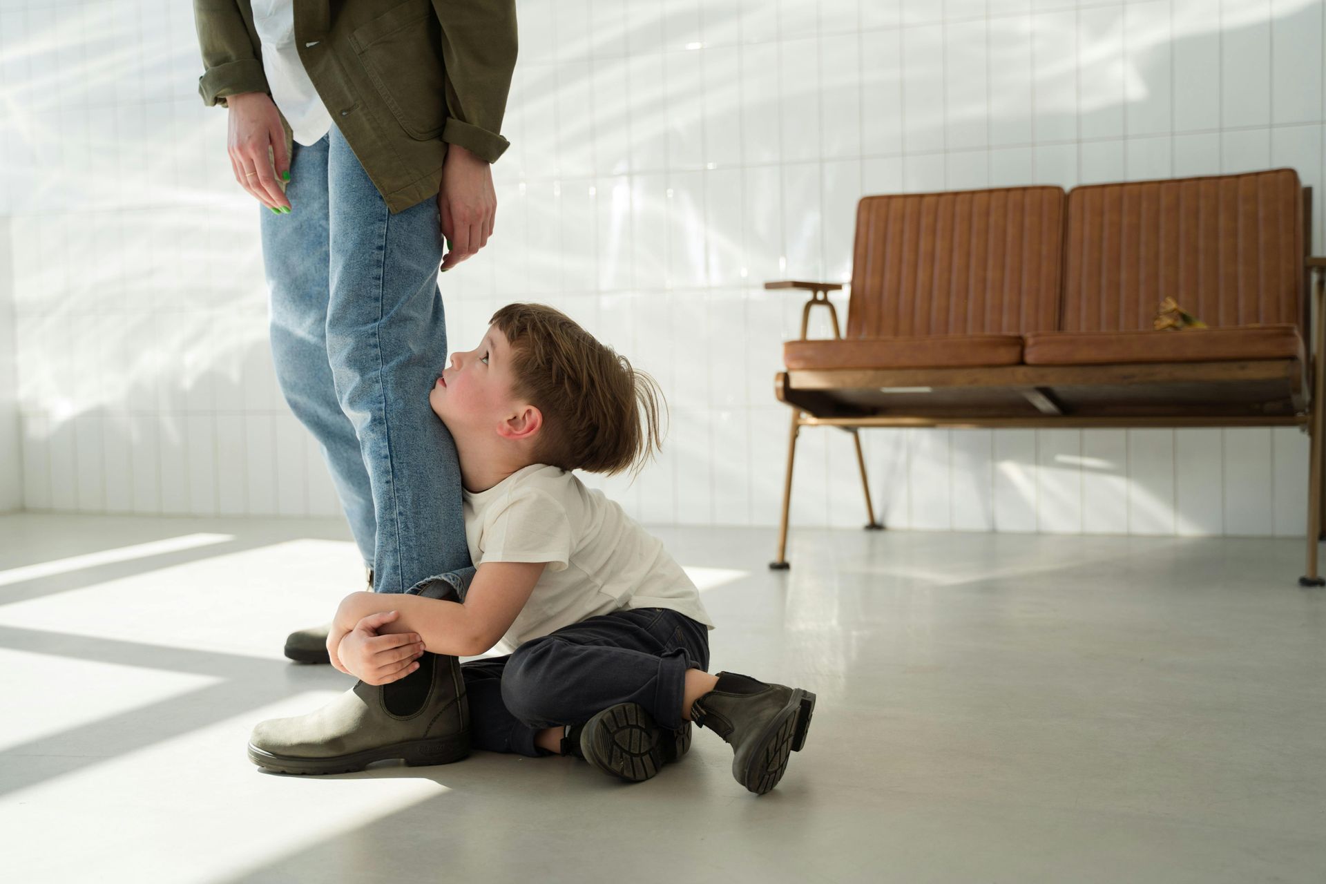 A little boy is sitting on the floor next to a man 's leg.