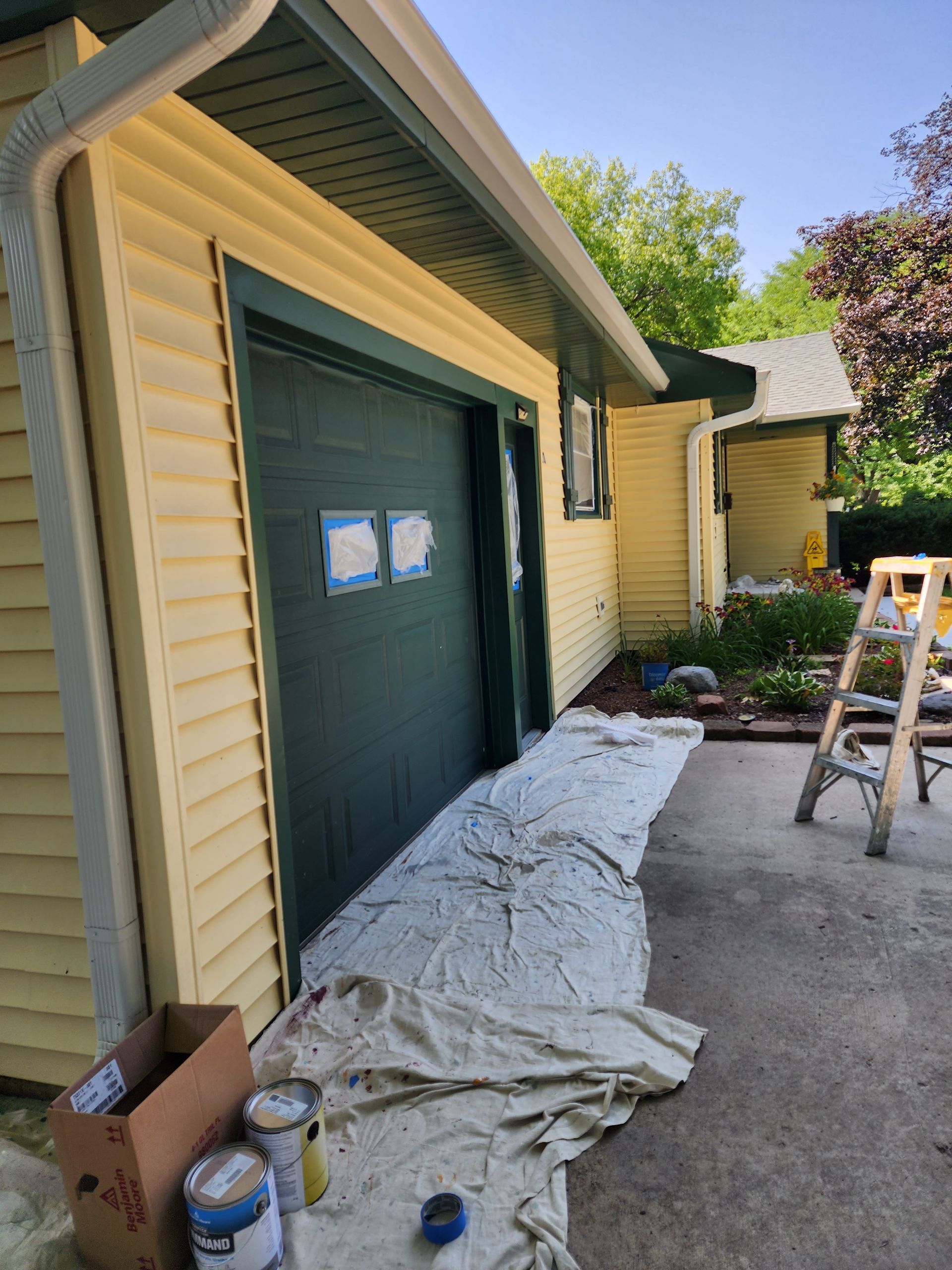 A yellow house with a green garage door is being painted.