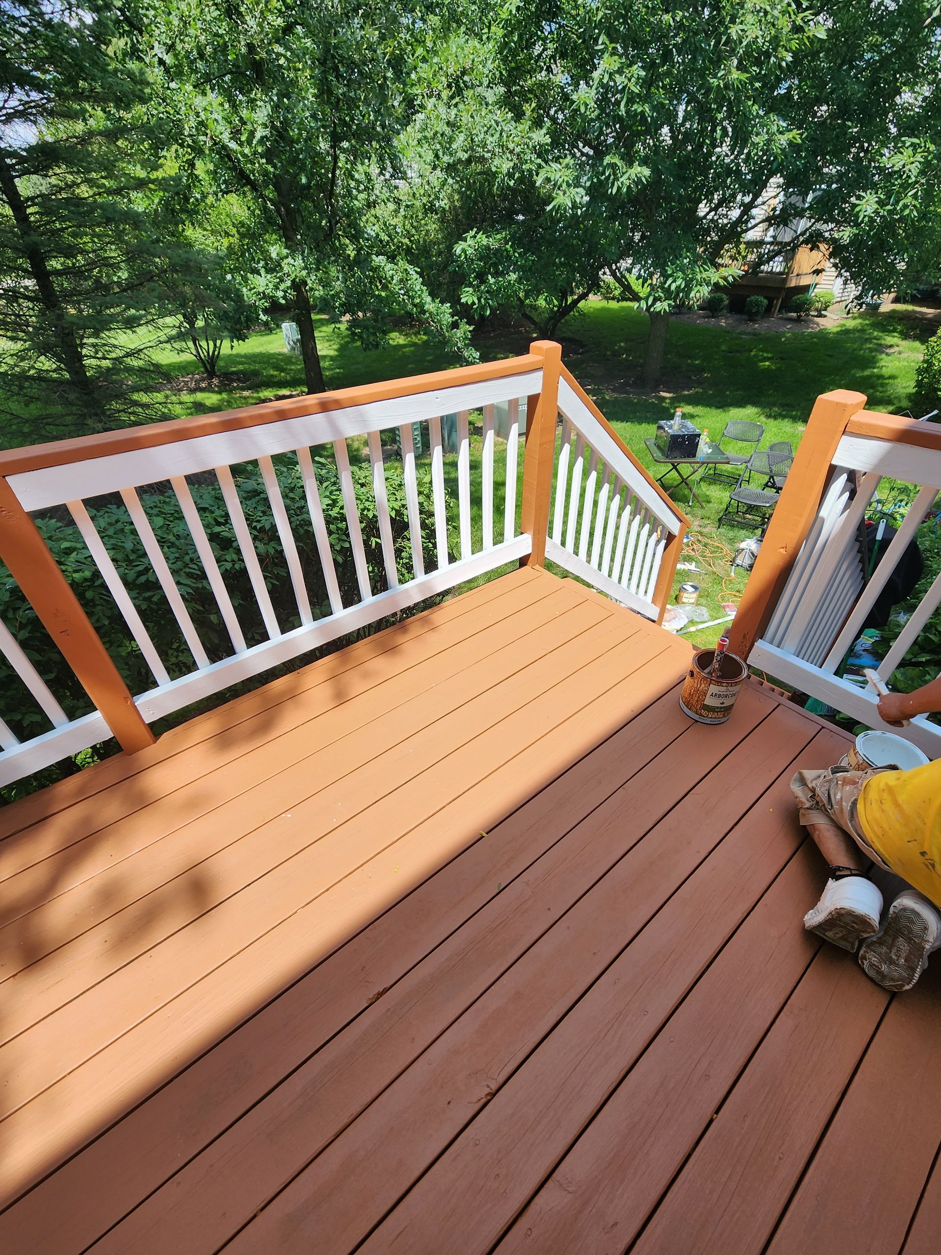 A person is sitting on a wooden deck with a white railing.