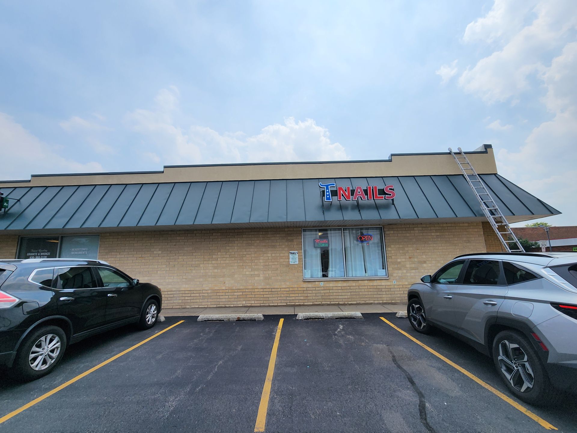 Two cars are parked in front of a building with a metal roof.