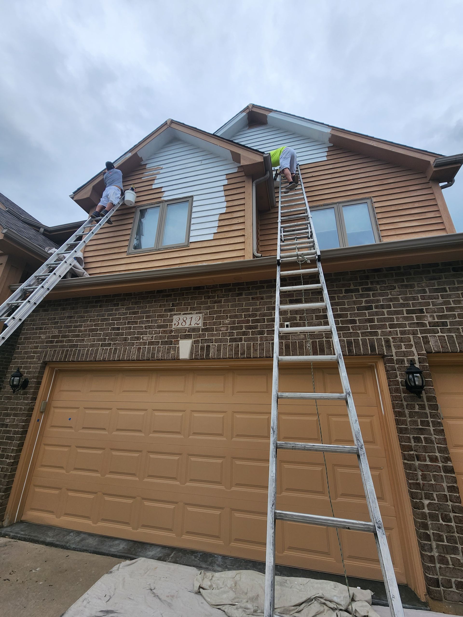 A man on a ladder is painting the side of a house.