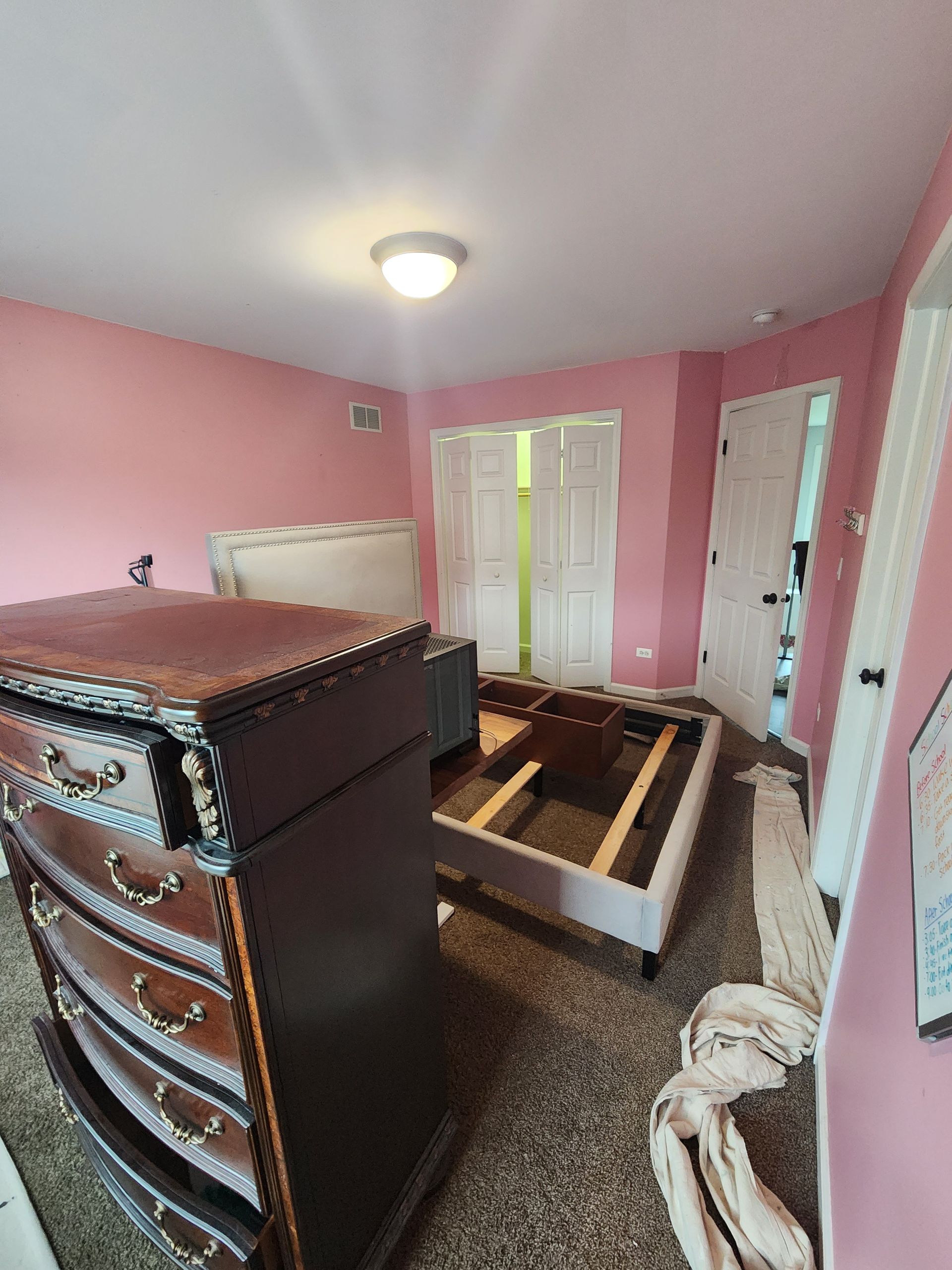 A bedroom with pink walls , a dresser and a bed.
