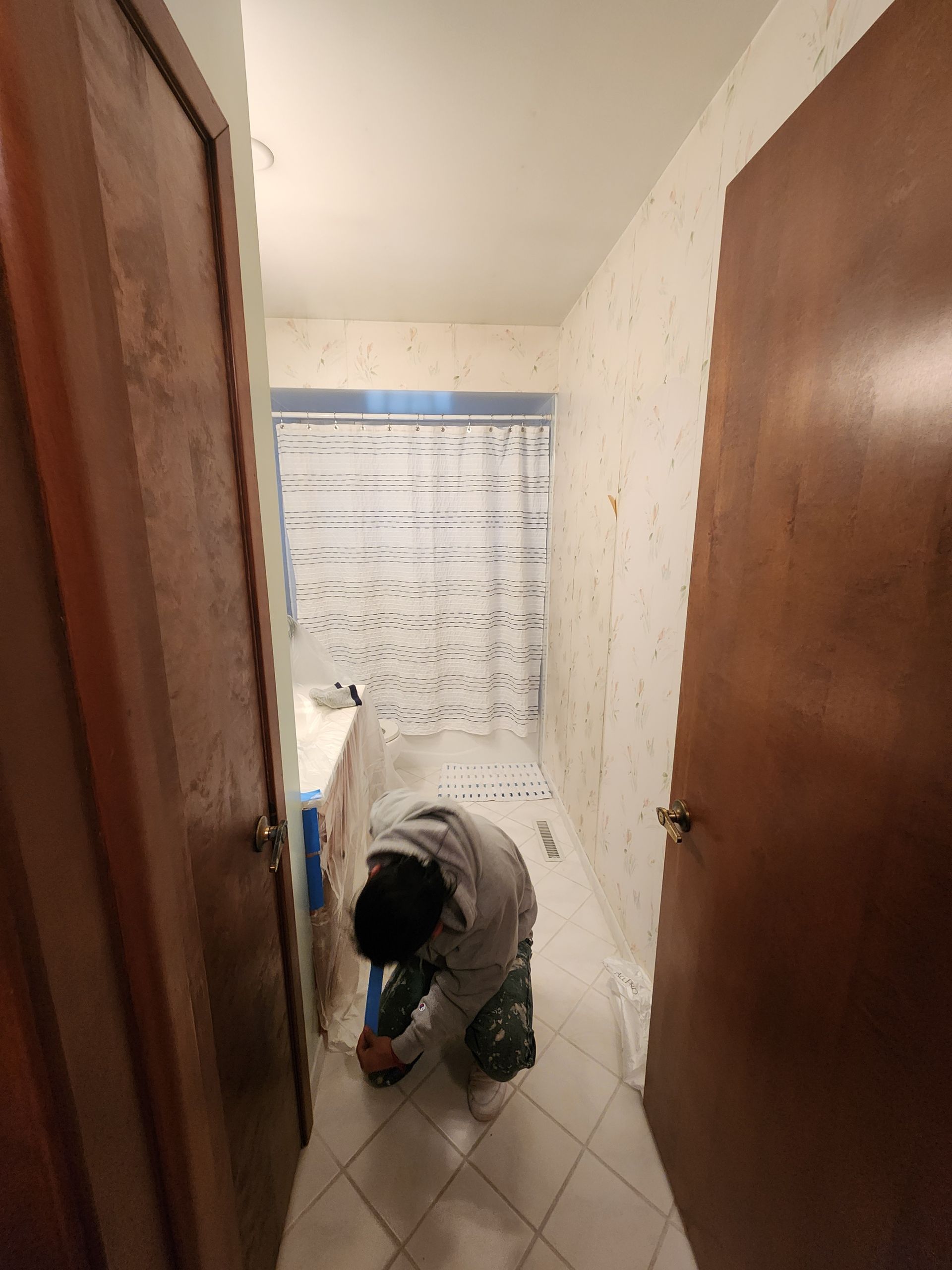 A man is kneeling down in a bathroom cleaning the floor.