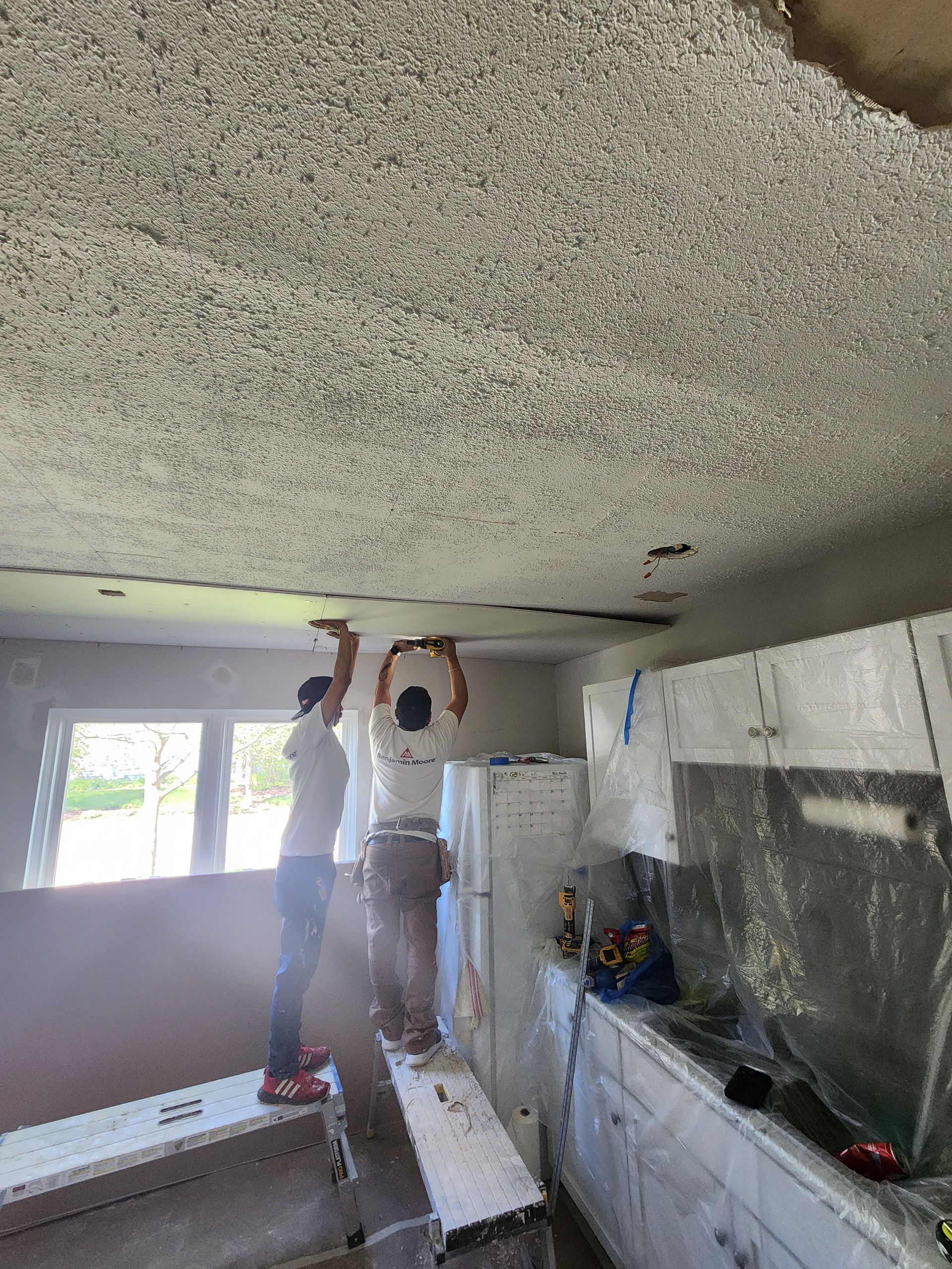 Two men are working on the ceiling of a kitchen.