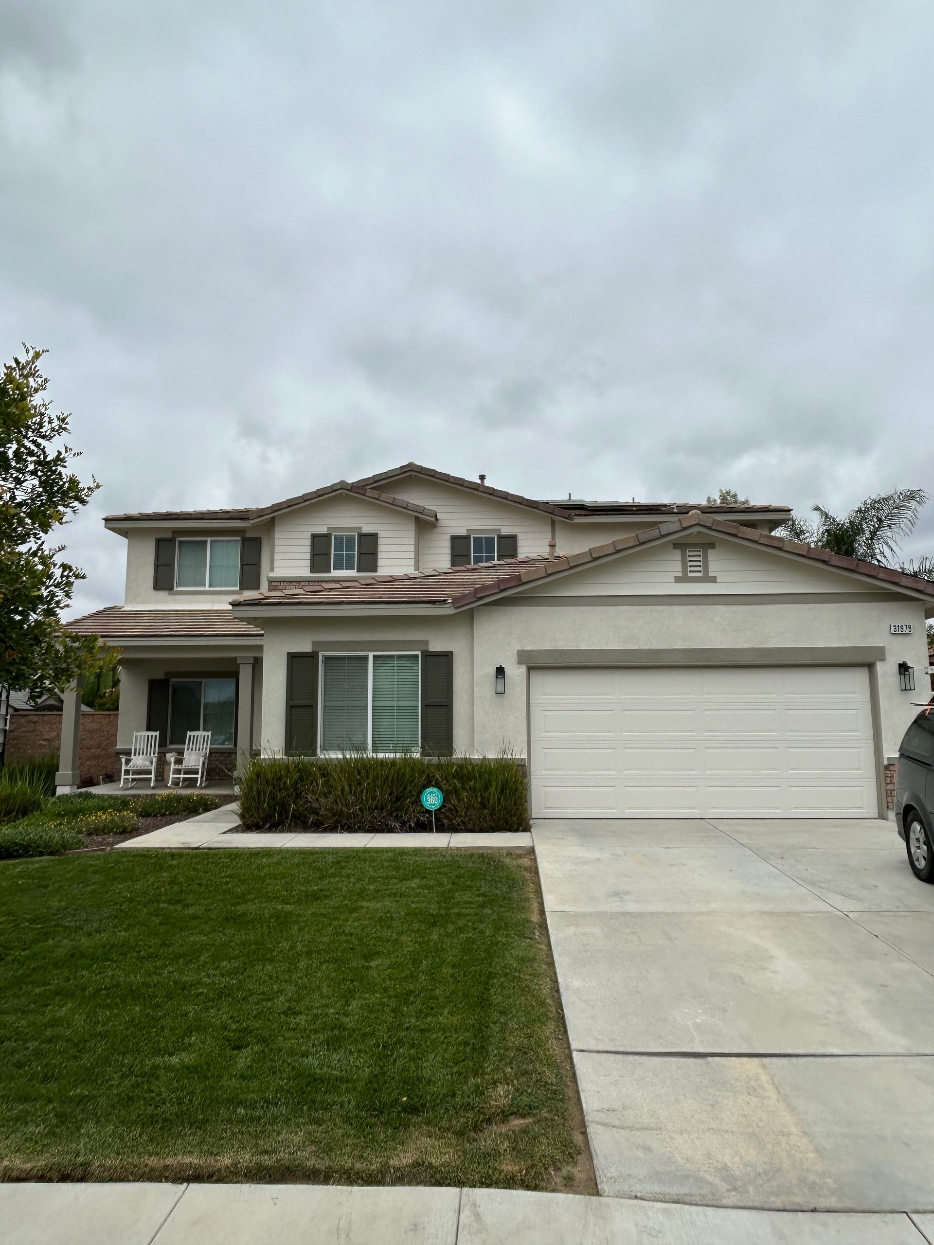 Two-story suburban house with a white garage, driveway, and trimmed front lawn under cloudy skies