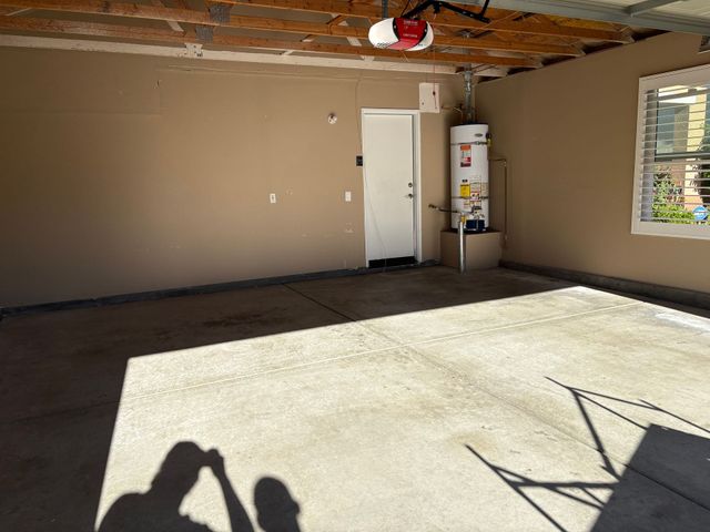 Empty garage with beige walls, exposed ceiling, open door, and sunlight on the concrete floor.