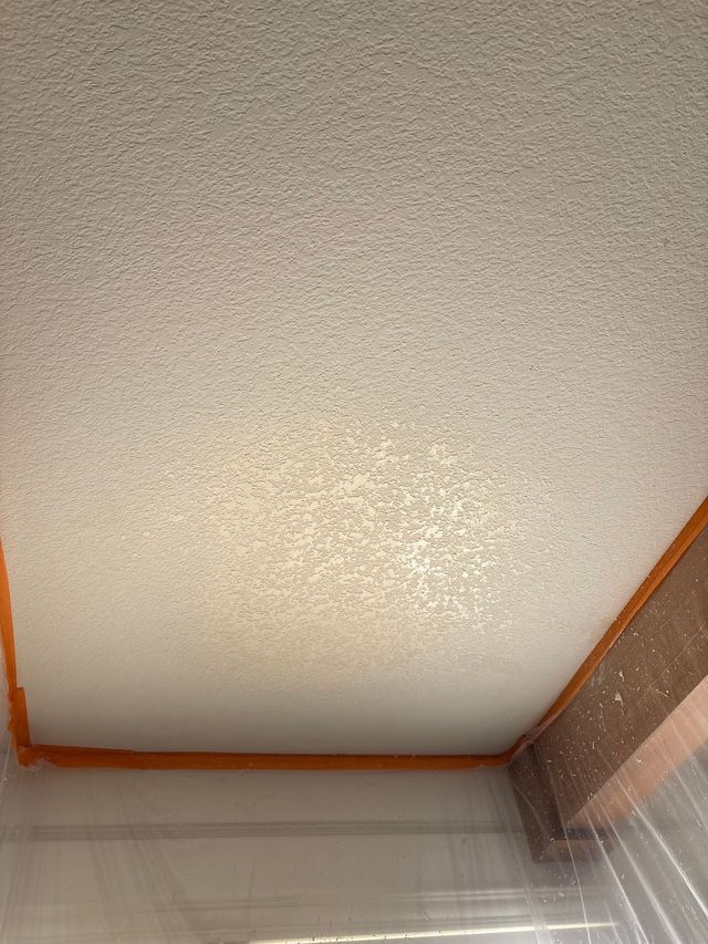 Textured white ceiling with orange trim above a room corner and sheer curtain below