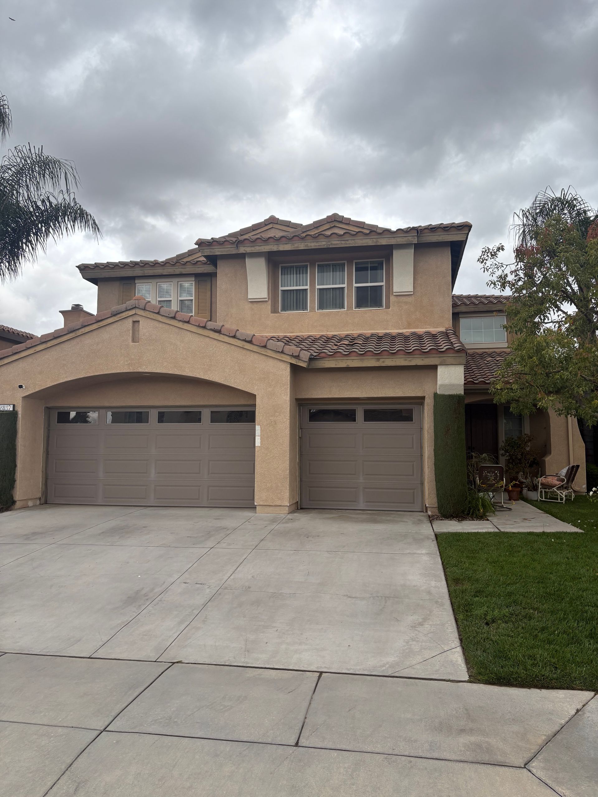 Two-story suburban house with beige stucco, a three-car garage, and a cloudy sky
