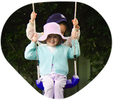 Two children on a swing. One in a blue sweater smiles, the other in a hat holds the ropes.