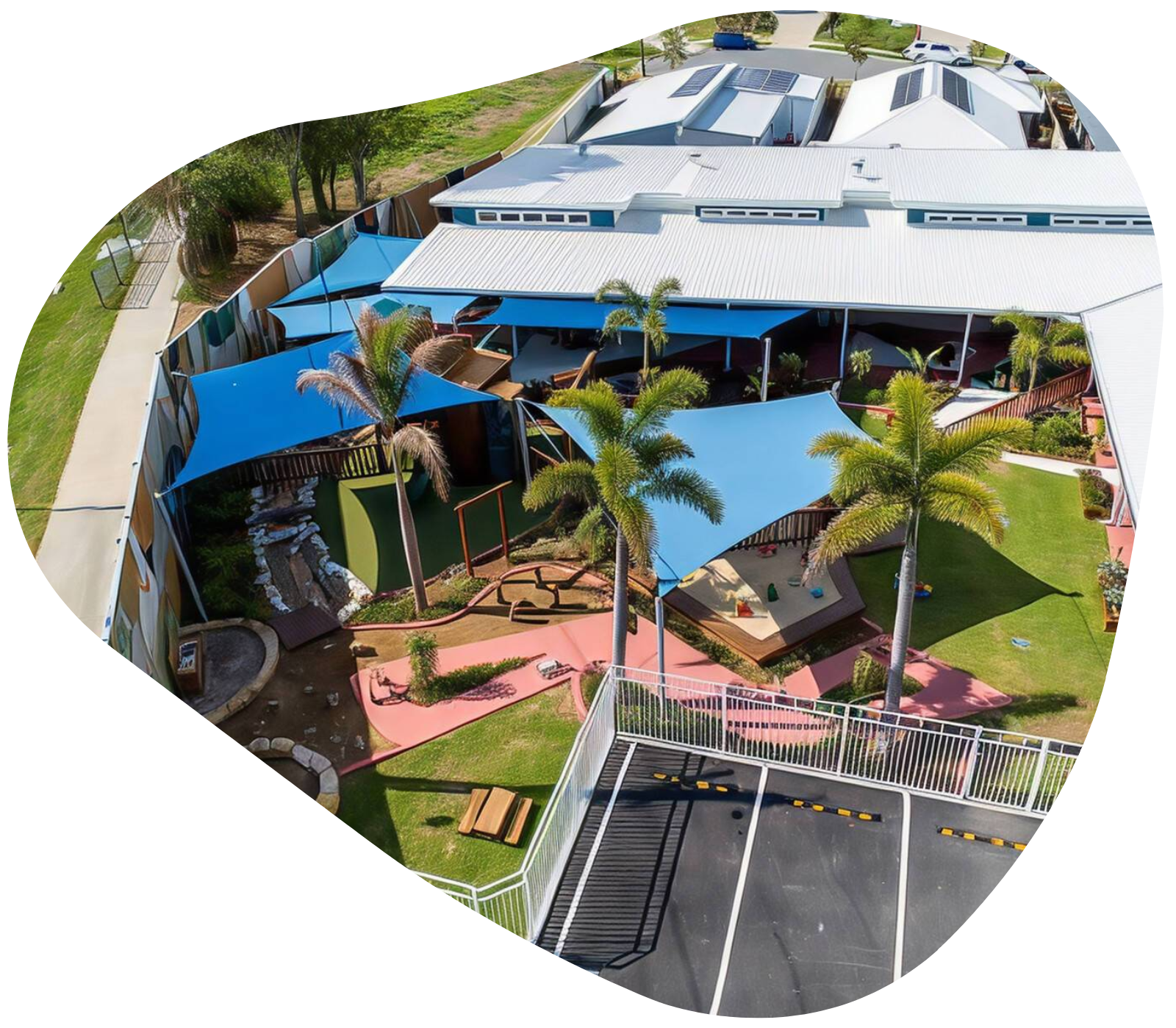 Aerial view of a daycare facility with blue shade sails, green grass, and a parking lot.