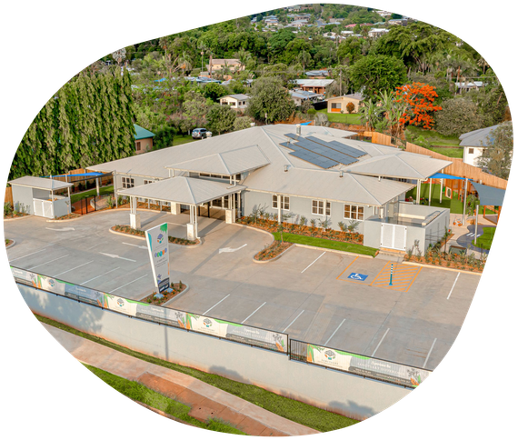 Aerial view of a light-colored building with solar panels, surrounded by a parking lot and greenery.