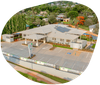 Aerial view of a light-colored building with solar panels, a parking lot, and surrounding greenery.