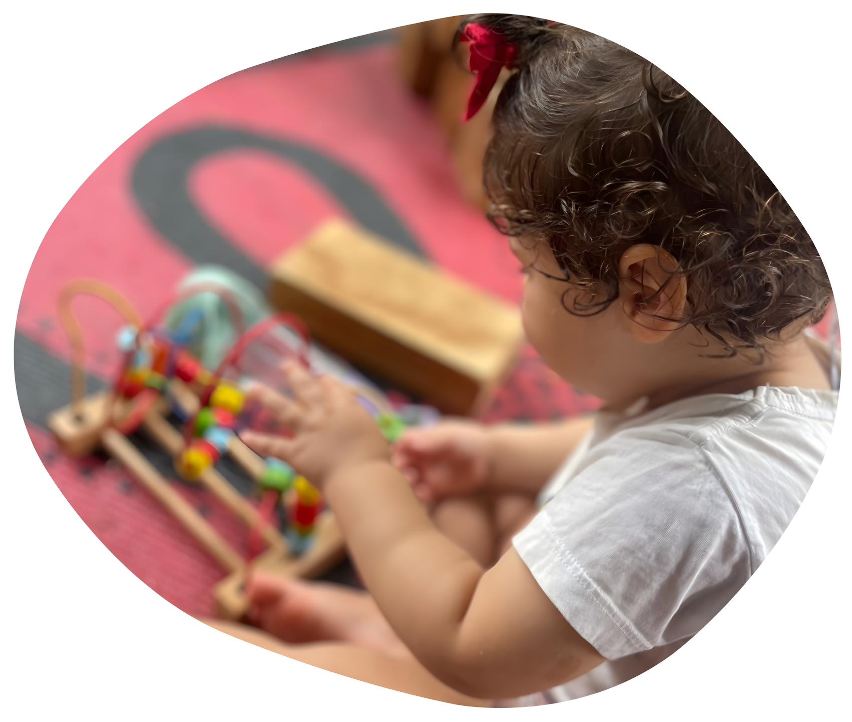 Child playing with a bead maze toy. Pink, red and black patterned mat in background.