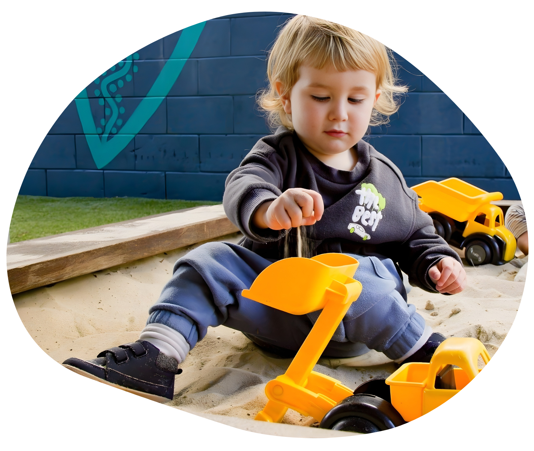 Child playing in a sandbox with yellow toy trucks.