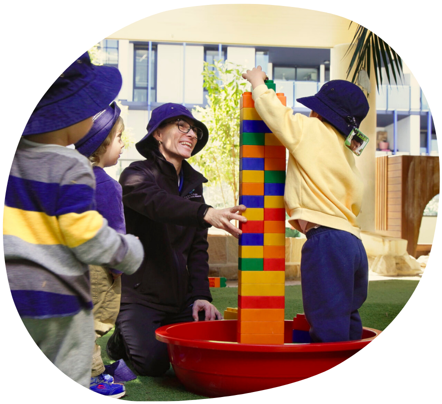 Children and adult building tower with large blocks in outdoor setting.