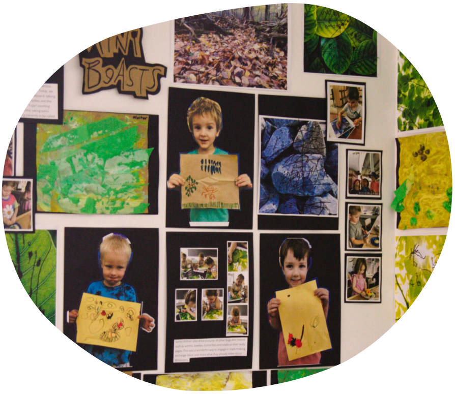 Children's artwork and photos on a wall. One child holds a brown paper drawing.