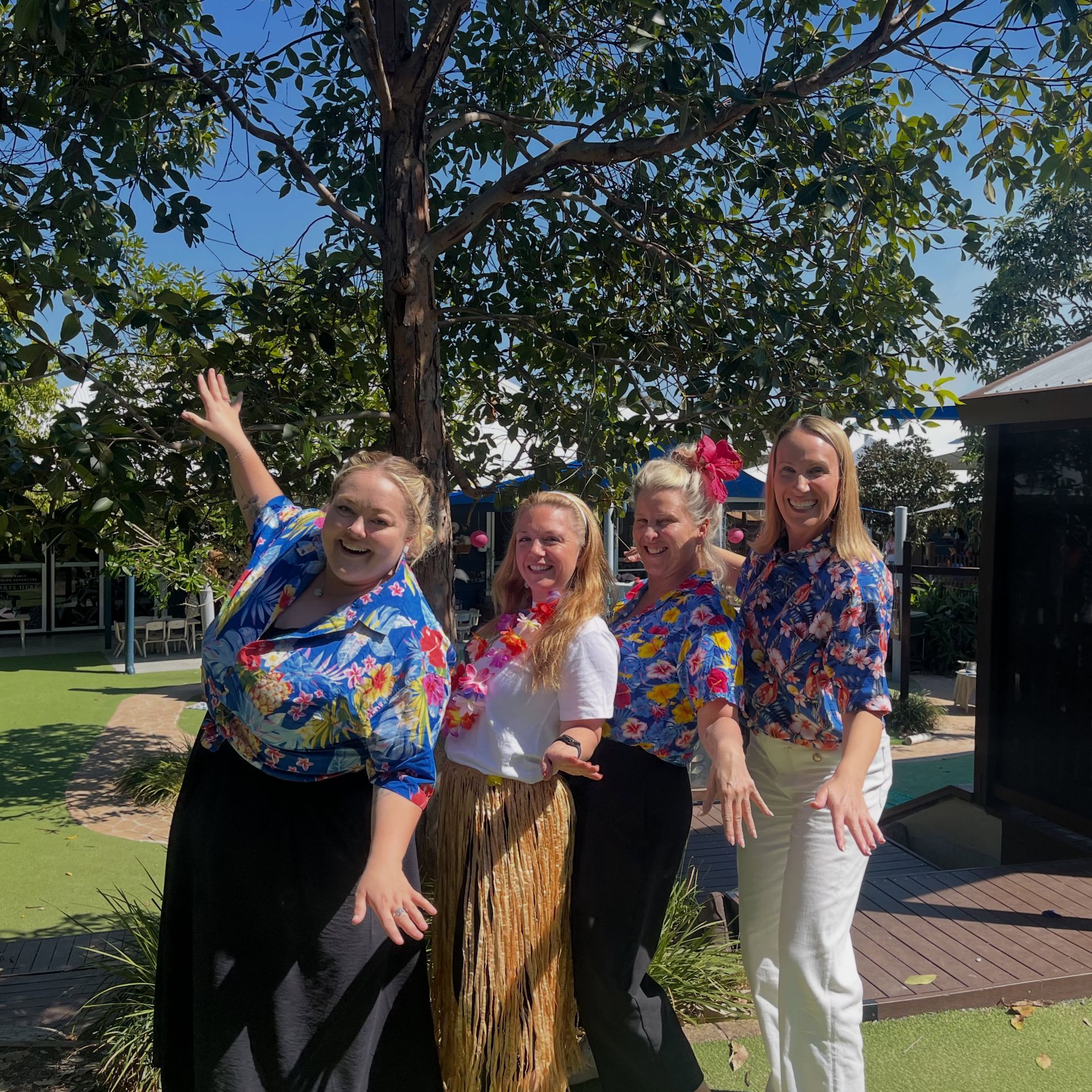 Four people dressed in hawaiian shirts pretending to surf a surfboard together