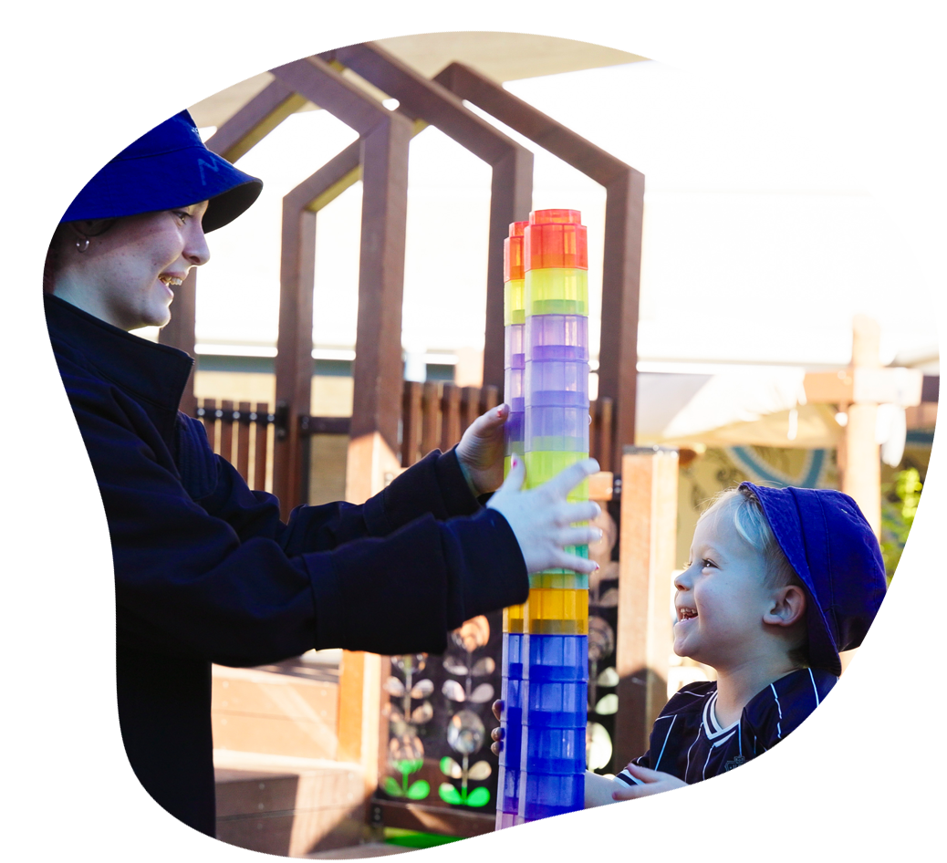 Woman and smiling child build a block tower outside.